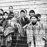 A group of child survivors behind a barbed wire fence at the Nazi concentration camp at Auschwitz-Birkenau in southern Poland, on the day of the camp’s liberation by the Red Army on Jan. 27, 1945. The photo was taken by Red Army photographer Captain Alexander Vorontsov during the making of a film about the liberation of the camp. The children were dressed in adult uniforms by the Russians. The children are (left to right): Tomy Schwarz (later Shacham), Miriam Ziegler, Paula Lebovics (front), Ruth Webber, Berta Weinhaber (later Bracha Katz), Erika Winter (later Dohan), Marta Weiss (later Wise), Eva Weiss (later Slonim), Gabor Hirsch (just visible behind Eva Weiss), Gabriel Neumann, Robert Schlesinger (later Shmuel Schelach), Eva Mozes Kor, and Miriam Mozes Zeiger.