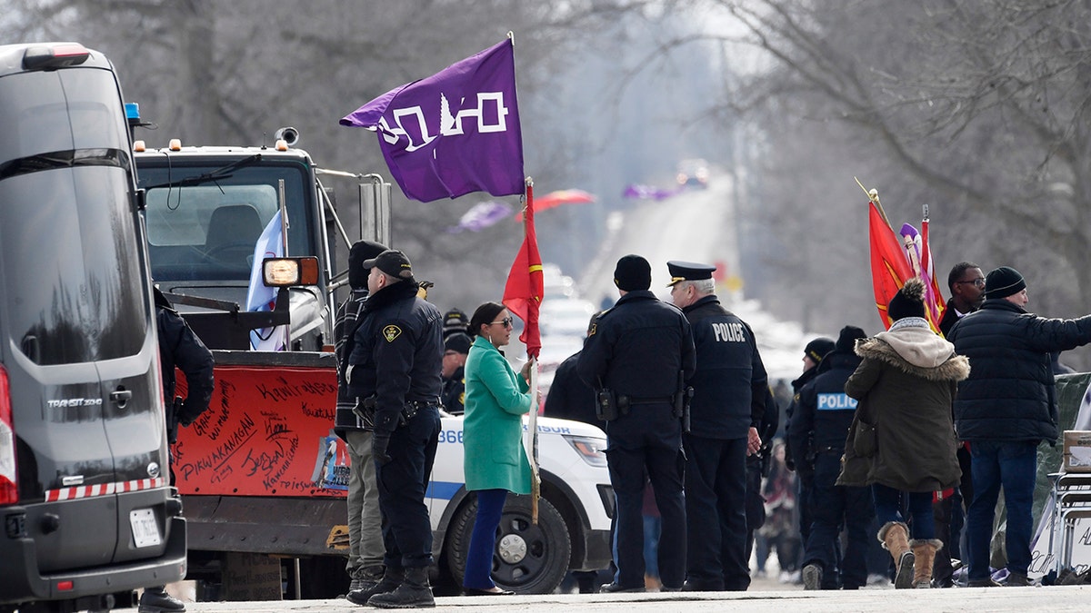 A woman speaks with Ontario Provincial Police officers as she removes flags from a rail blockade in Tyendinaga Mohawk Territory, near Belleville, Ont., on Monday Feb. 24, 2020, during a protest in solidarity with Wet'suwet'en Nation hereditary chiefs attempting to halt construction of a natural gas pipeline on their traditional territories. (Adrian Wyld/The Canadian Press via AP)