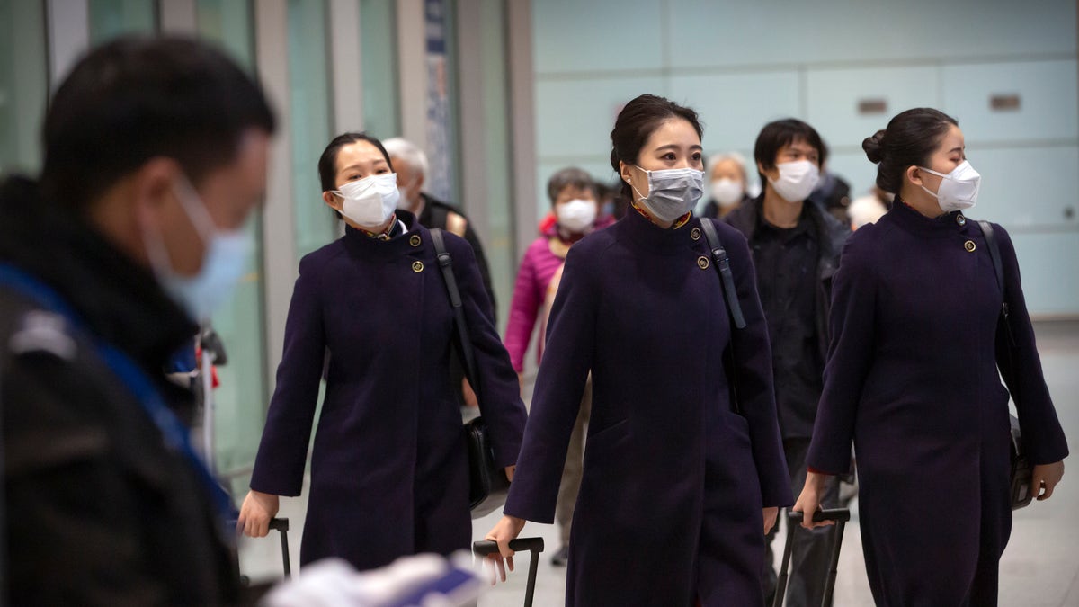 Flight crew members wearing face masks walk through the international arrivals area at Beijing Capital International Airport on Jan. 30. (AP Photo/Mark Schiefelbein)