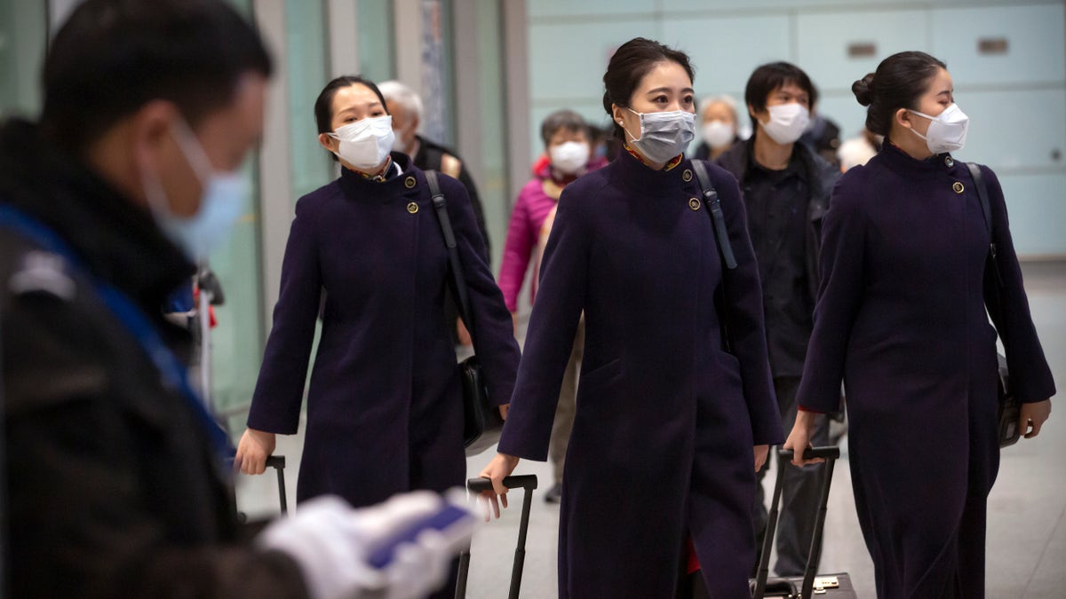 Flight crew members wearing face masks walk through the international arrivals area at Beijing Capital International Airport on Jan. 30. (AP Photo/Mark Schiefelbein)