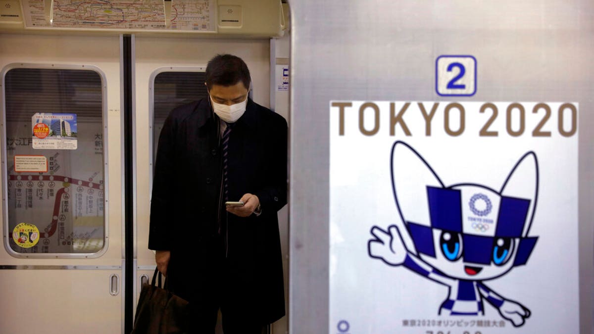 A poster promoting the Tokyo 2020 Olympics is posted next a train door as a commuter wearing a mask looks at his phone in a train, Friday, Jan. 31, 2020, in Tokyo. 