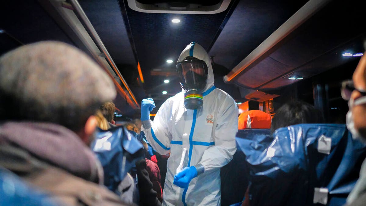 A military officer wearing a protective suit gives instructions to evacuees from Wuhan, China, as they travel to a hospital after their arrival at a military base in Wroclaw, Poland, on Feb. 2, 2020. (AP Photo/Arek Rataj, File)
