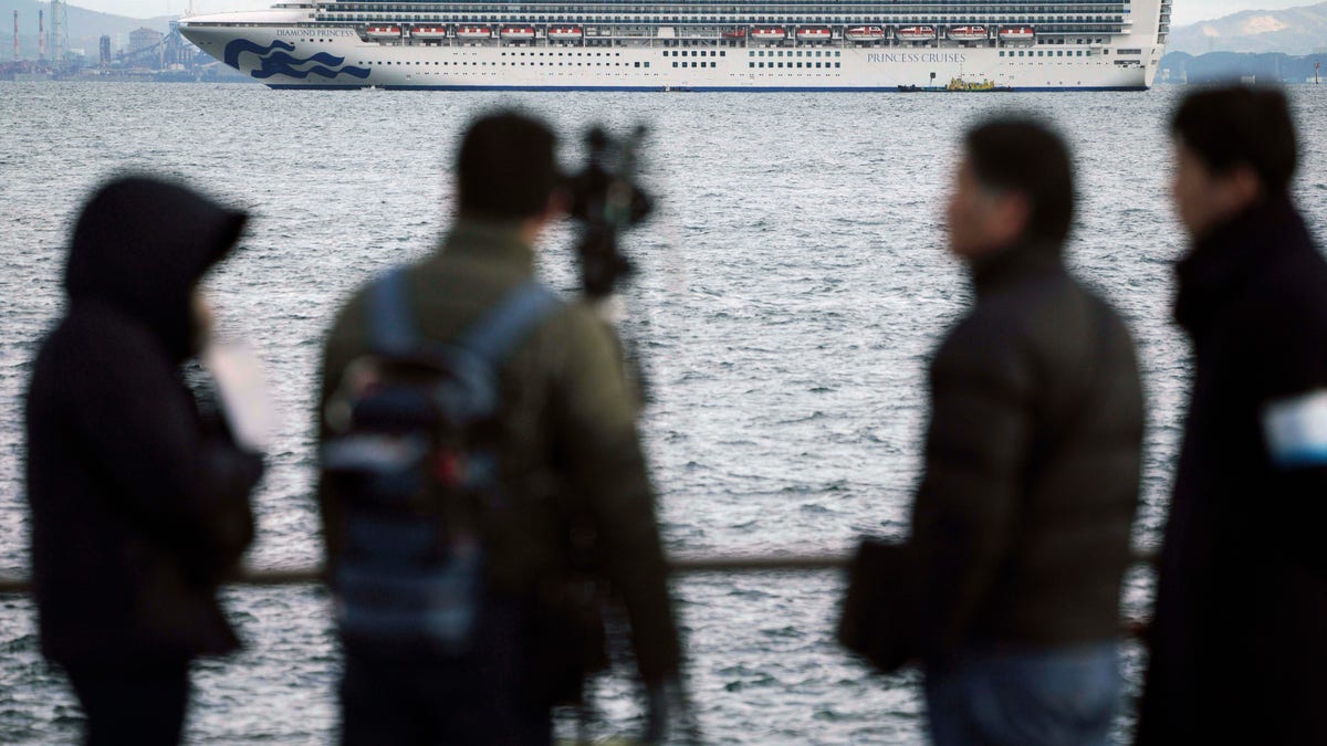 A TV crew film a cruise ship Diamond Princess anchoring off the Yokohama Port Tuesday, Feb. 4, 2020. (AP Photo/Eugene Hoshiko)