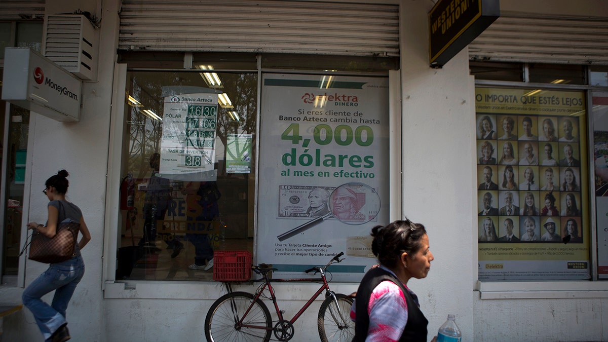 FILE - In this April 5, 2016 file photo, pedestrians walk past signs advertising money transfer services and loans, outside a business in Mexico City. Mexican migrants working abroad sent home a record $36 billion in remittances in 2019, the country's central bank reported Tuesday, Feb. 4, 2020. (AP Photo/Rebecca Blackwell, File)