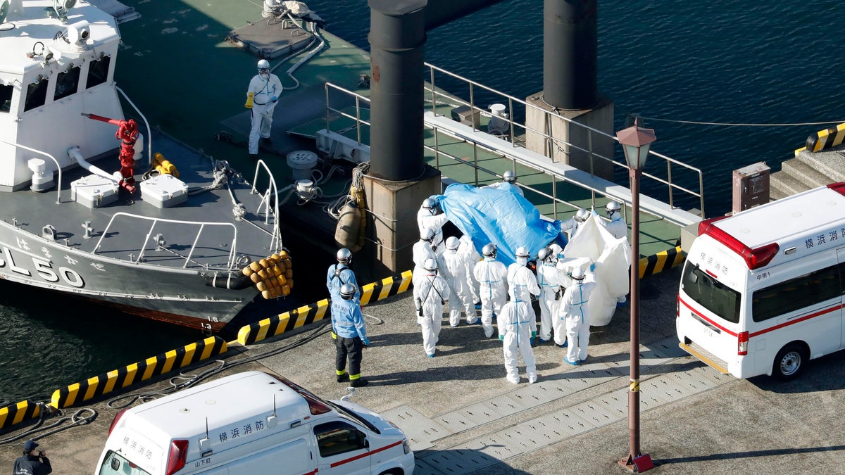 Medical workers in protective suits lead a passenger tested positive for a new coronavirus from the cruise ship Diamond Princess at Yokohama Port in Yokohama, south of Tokyo, Wednesday, Feb. 5, 2020. Japan said Wednesday 10 people on the cruise ship have tested positive for the new virus and were being taken to hospitals. (Hiroko Harima/Kyodo News via AP)