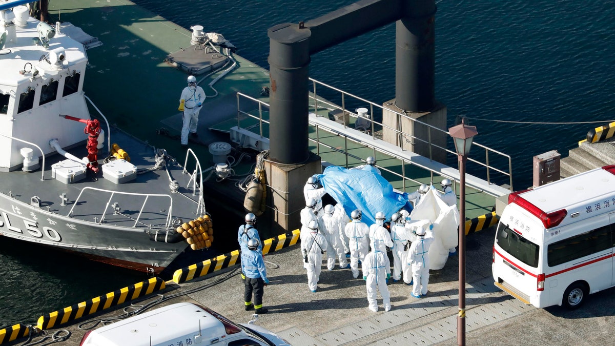 Medical workers in protective suits lead a passenger tested positive for a new coronavirus from the cruise ship Diamond Princess at Yokohama Port in Yokohama, south of Tokyo, Wednesday, Feb. 5, 2020.. (Hiroko Harima/Kyodo News via AP)