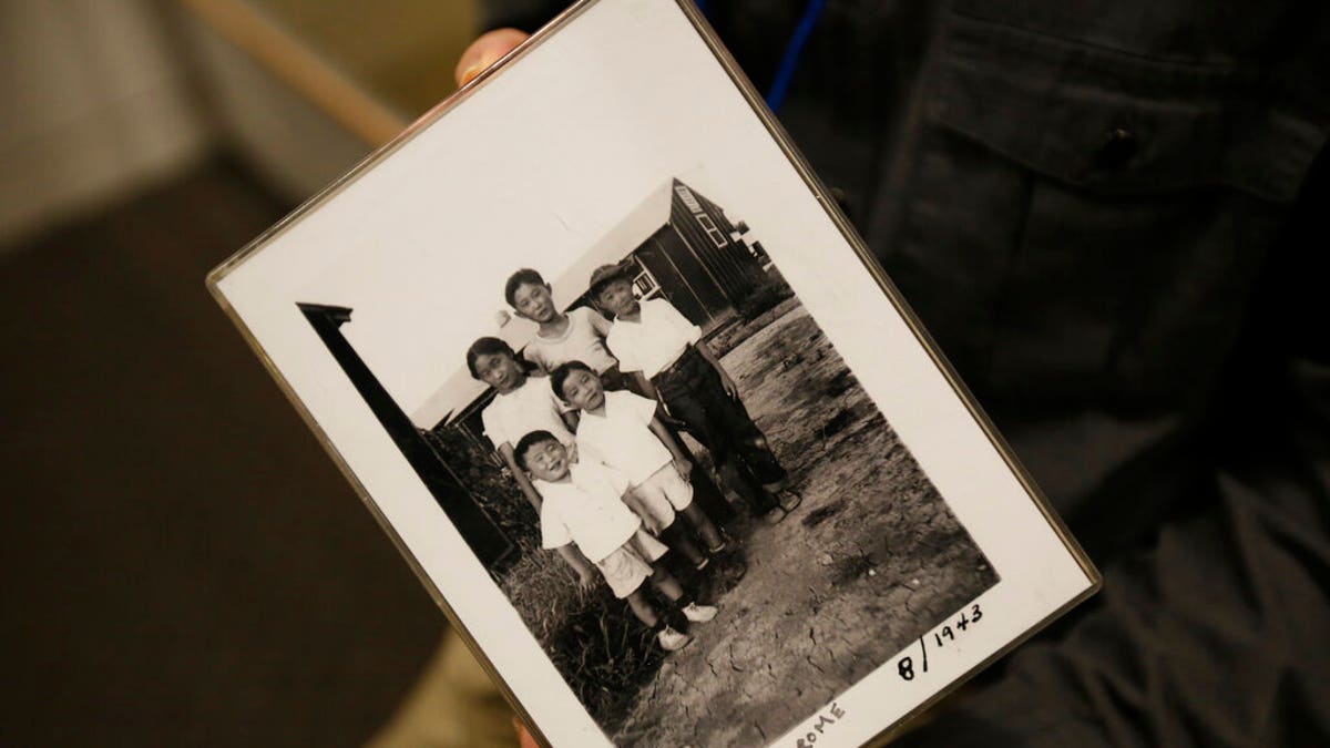 In this photo taken Tuesday, Feb. 11, 2020, Les Ouchida holds a 1943 photo of himself, front row, center, and his siblings taken at the internment camp his family was moved to, as he poses at the permanent exhibit titled "UpRooted Japanese Americans in World War II" at the California Museum in Sacramento, Calif.