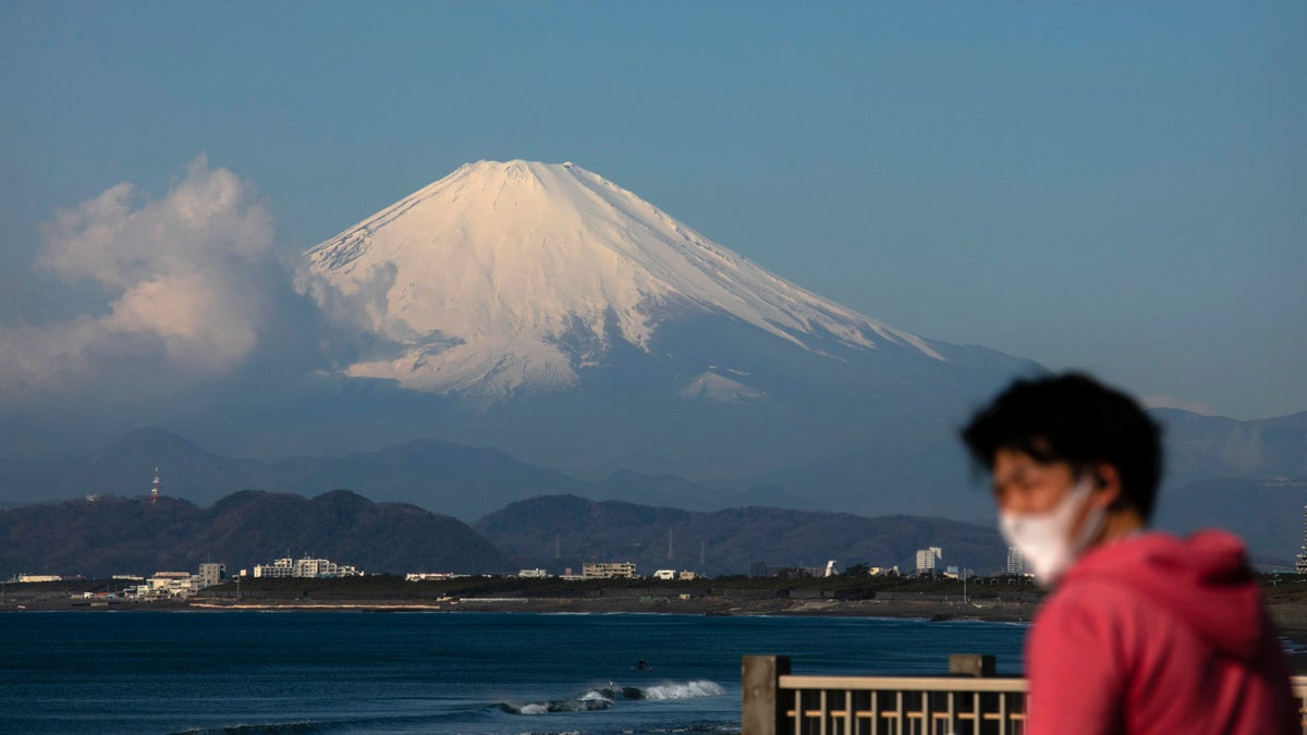 A man wearing a mask visits a beach as snow-capped Mount Fuji is visible in the distance in Fujisawa, Japan, Thursday, Feb. 27, 2020. According to local businesses in the area, the number of visitors has dropped significantly since the outbreak of COVID-19. (AP Photo/Jae C. Hong)