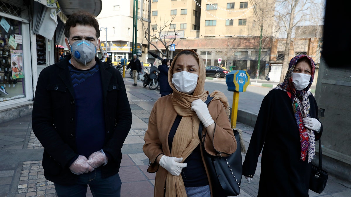 Tehran resident Leila Tayyeb, center, with her husband wearing mask and gloves, speaks with The Associated Press, as a woman walks past, in downtown Tehran, Iran, Thursday, Feb. 27, 2020.? (AP Photo/Vahid Salemi)