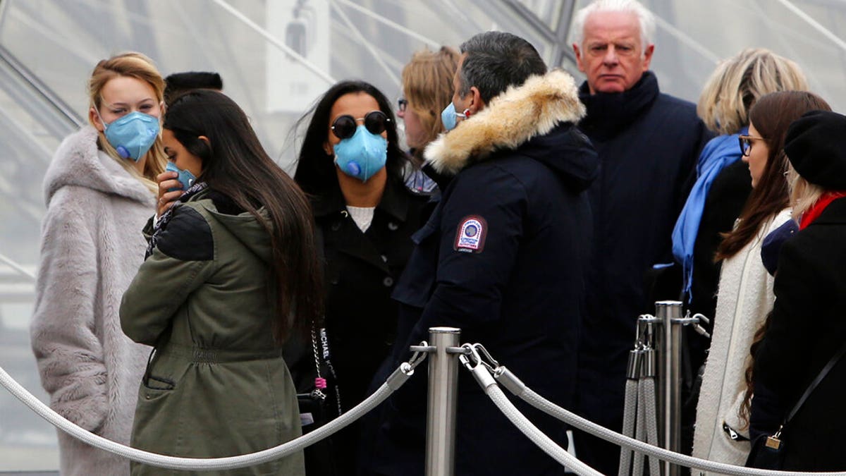 Tourists, some wearing a mask, queue to enter the Louvre museum Friday, Feb. 28, 2020 in Paris.