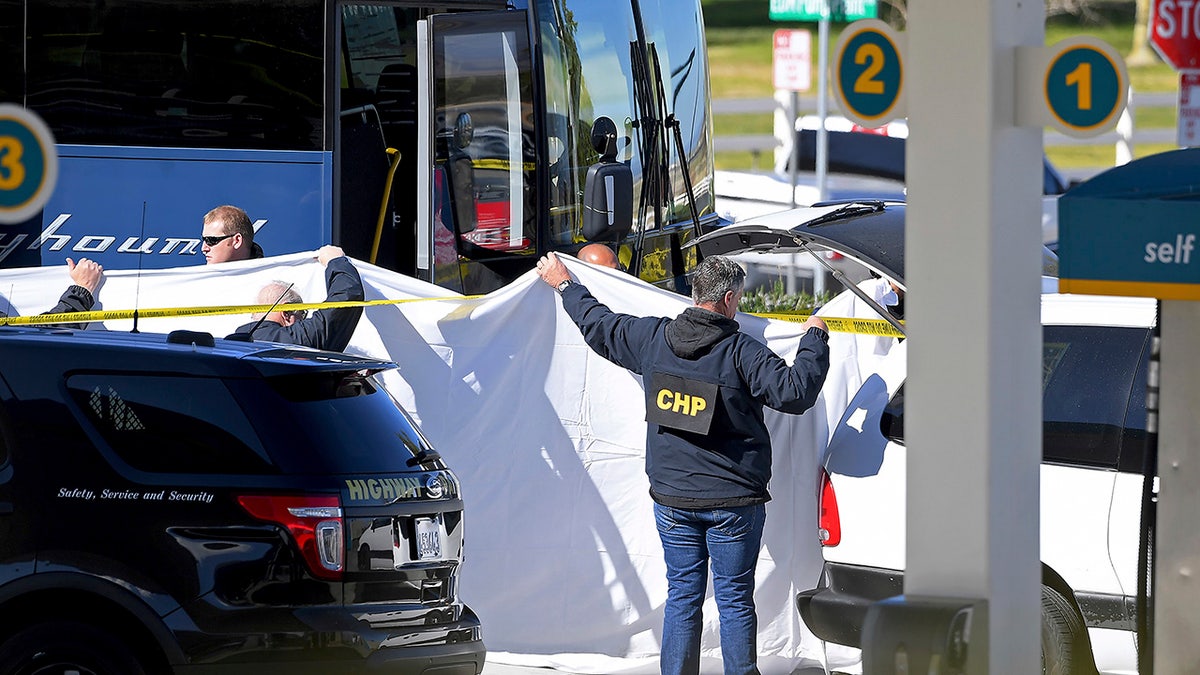 Coroner's officials work behind a drape to remove the body of a person who was killed when a gunman opened fire aboard a packed Greyhound bus, and wounded five others before the driver pulled over onto the shoulder and the killer got off, in Lebec, Calif., Monday. (AP Photo/Jayne Kamin-Oncea)