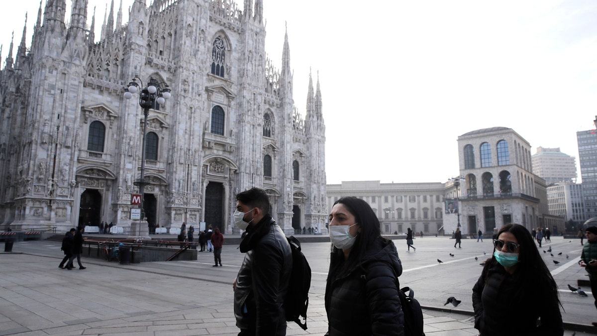 People wearing sanitary masks walk past the Duomo gothic cathedral in Milan, Italy, Sunday, Feb. 23, 2020.