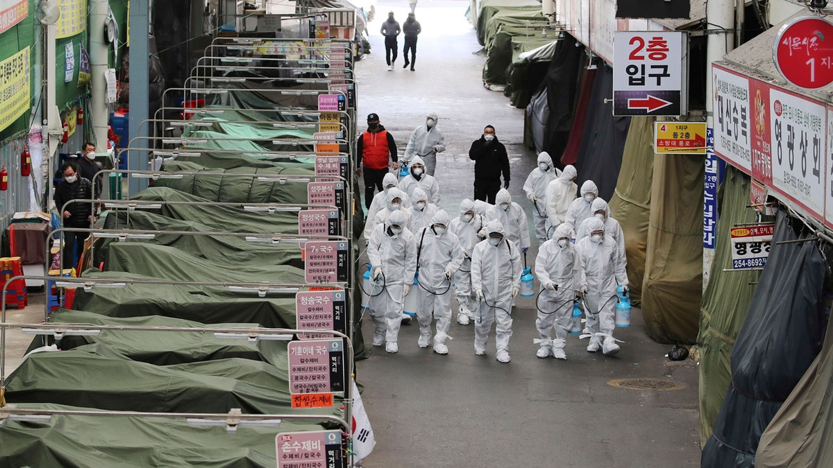 Workers wearing protective gear spray disinfectant as a precaution against the COVID-19 coronavirus in a local market in Daegu, South Korea, Sunday, Feb. 23, 2020.