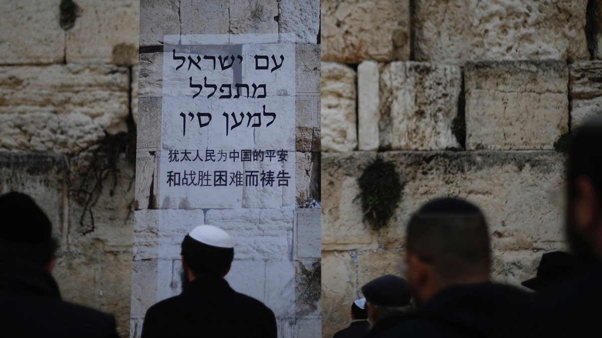 Jews pray at the Western Wall, the holiest site where Jews can pray in Jerusalem's Old City, Sunday, Feb. 16, 2020. As concerns over the coronavirus's spread rise, Jewish faithful held a prayer session Sunday at the Western Wall in search of divine intervention to help stave off contagious disease. Poster in Hebrew and Chinese says, "The People of Israel pray for China." (AP Photo/Ariel Schalit)
