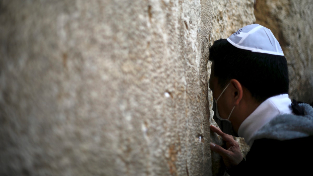 A man with a mask on his face prays at the Western Wall, the holiest site where Jews can pray in Jerusalem's Old City, Sunday, Feb. 16, 2020. As concerns over the coronavirus's spread rise, Jewish faithful held a prayer session Sunday at the wall in search of divine intervention to help stave off the contagious disease. (AP Photo/Ariel Schalit)