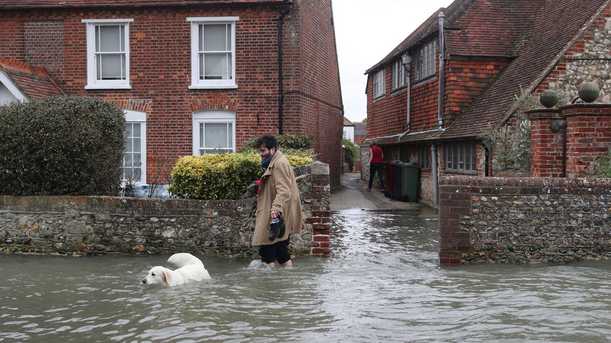 A man walks with a dog in flood water, in the aftermath of Storm Ciara, in Bosham, Sussex , England, Monday Feb. 10, 2020.