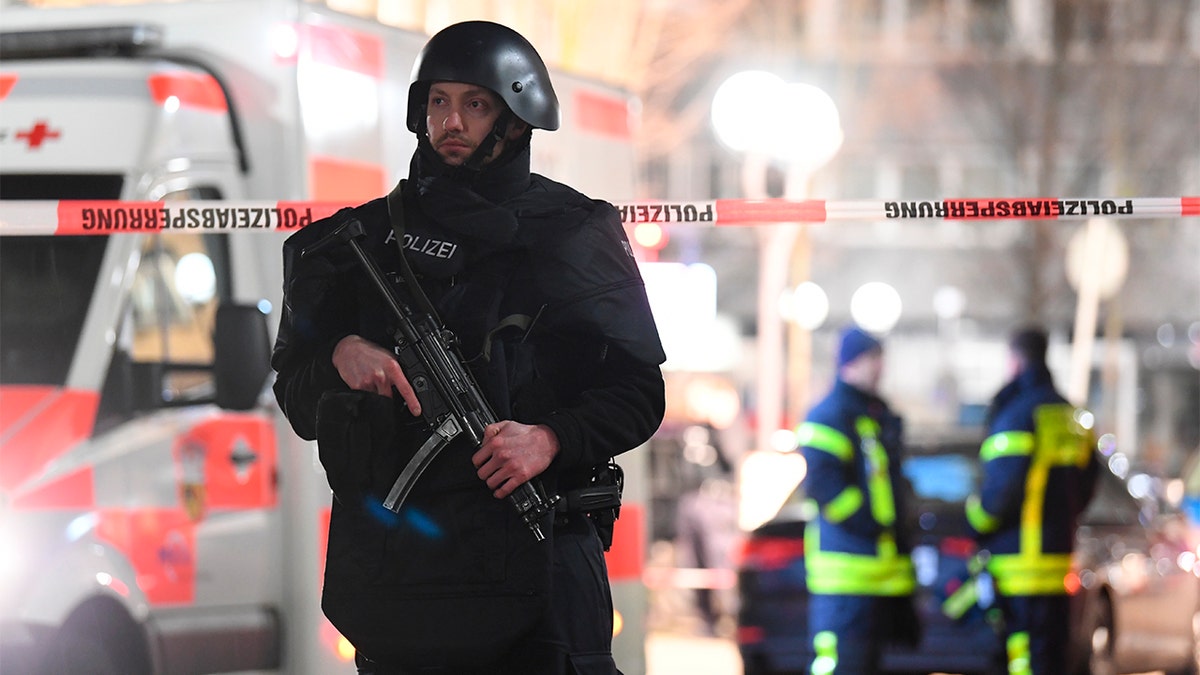 A police officer stands guard near the scene in front of a restaurant after a shooting in central Hanau, Germany Thursday, Feb. 20, 2020. Eight people were killed in shootings in the German city of Hanau on Wednesday evening, authorities said. (Boris Roessler/dpa via AP)