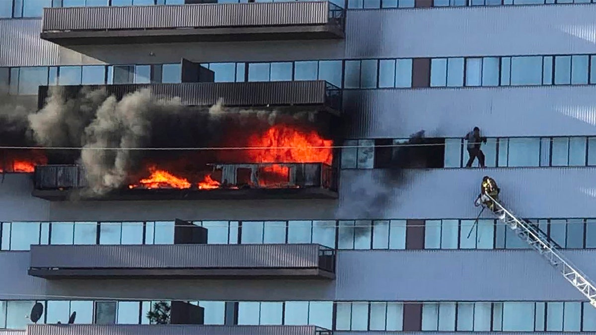 This image from video by Jenna Fabian shows a Los Angeles Fire Department firefighter on a ladder rescuing a man who had climbed out on the side of a 25-story high-rise apartment, escaping flames from a burning apartment balcony, after a fire broke out on a sixth-floor balcony and sent choking smoke billowing through the upper levels in West Los Angeles Wednesday, Jan. 29, 2020. (Courtesy of Jenna Fabian via AP)