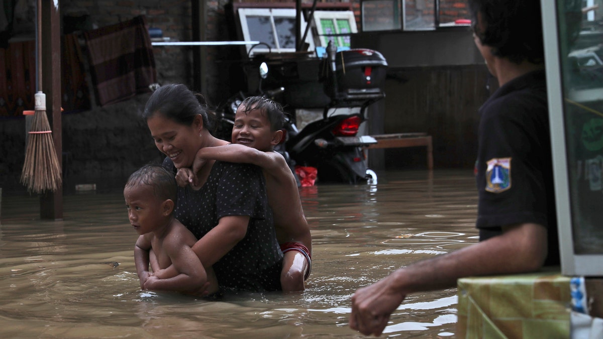 A woman carries her children through flood waters at a flooded neighborhood in Jakarta, Indonesia.