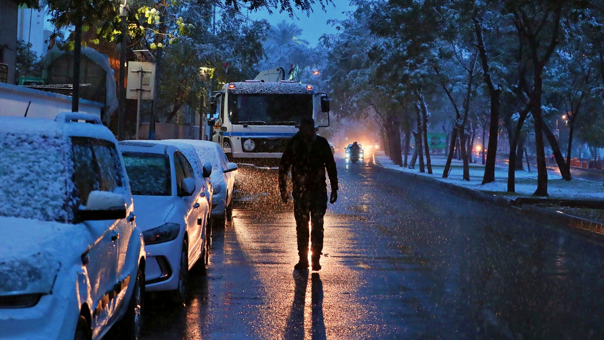 A man walks on a road while it snows in Baghdad, Iraq, Tuesday, Feb. 11, 2020.