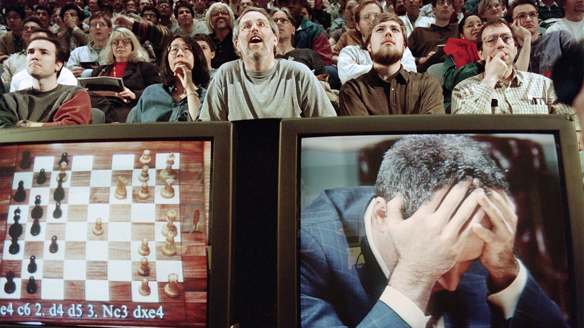 Chess enthusiasts watch World Chess champion Garry Kasparov on a television monitor as he holds his head in his hands at the start of the sixth and final match against IBM's Deep Blue computer in New York. Kasparov lost this match in just 19 moves giving overall victory to Deep Blue with a score of 2.5-3.5. / AFP / STAN HONDA (Photo credit should read STAN HONDA/AFP via Getty Images)