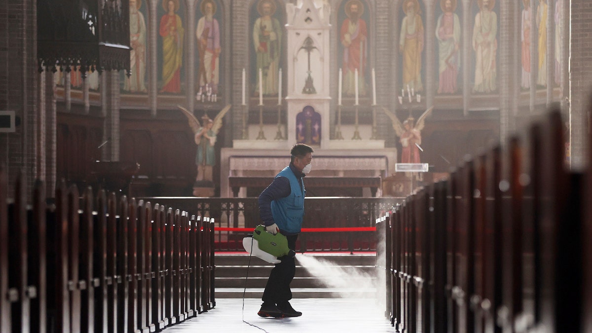 A worker wearing a face mask sprays disinfectant as a precaution against the new coronavirus at Myeongdong Cathedral in Seoul, South Korea, Wednesday, Feb. 26, 2020. (Lee Ji-eun/Yonhap via AP)