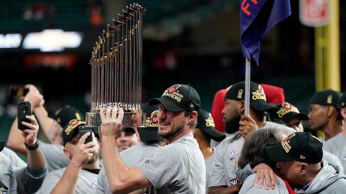 In this Oct. 30, 2019, file photo, Washington Nationals starting pitcher Max Scherzer celebrates with the trophy after Game 7 of the baseball World Series against the Houston Astros in Houston. The Nationals head to spring training with mostly the same squad that won the World Series. They are counting again on being led by a star-studded rotation featuring Scherzer and Stephen Strasburg, along with slugger Juan Soto. (AP Photo/David J. Phillip, File)
