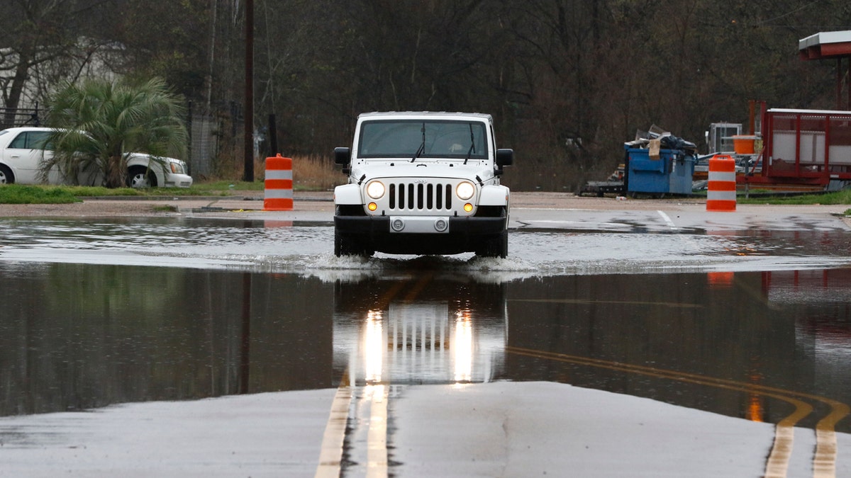 A vehicle carefully passes through a flooded street in downtown Jackson, Miss., as flooding from the Pearl River continues to impact several communities along its bank, Sunday, Feb. 16, 2020.