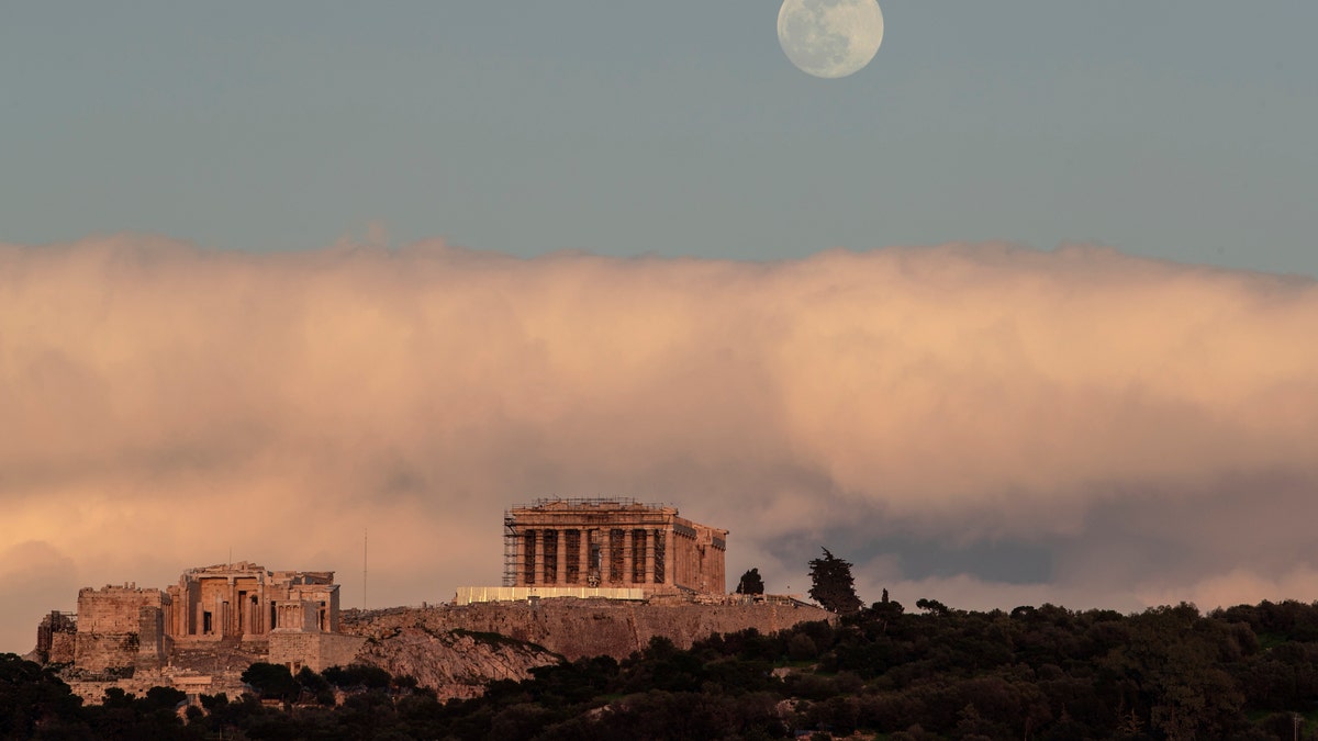 The moon rises behind the ancient Acropolis hill with the 500 BC Parthenon temple in Athens, on Saturday, Feb. 8, 2020.