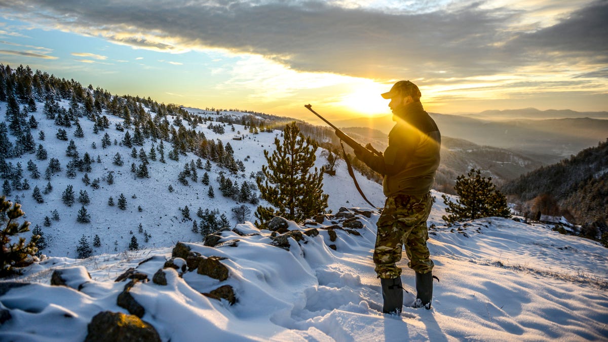 Hunter observing a beautiful vista while standing on a mountain ridge covered with snow