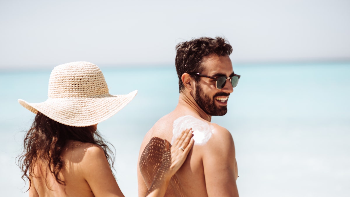 Woman rubbing sunscreen on a mans back
