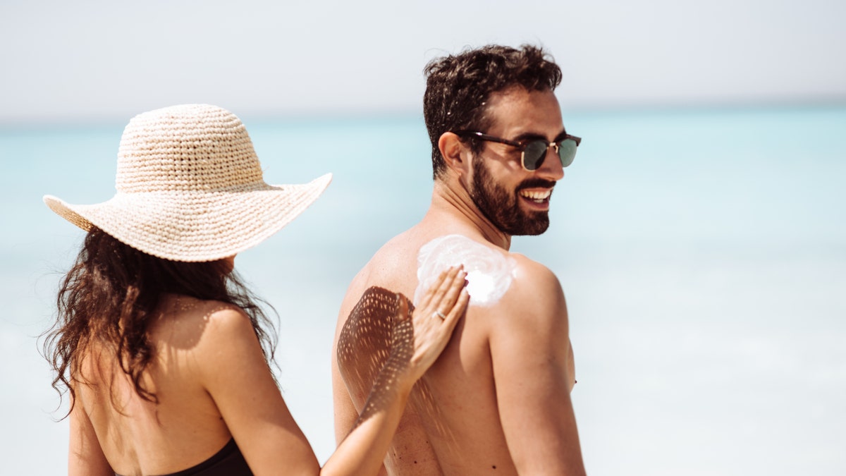 Woman rubbing sunscreen on a mans back