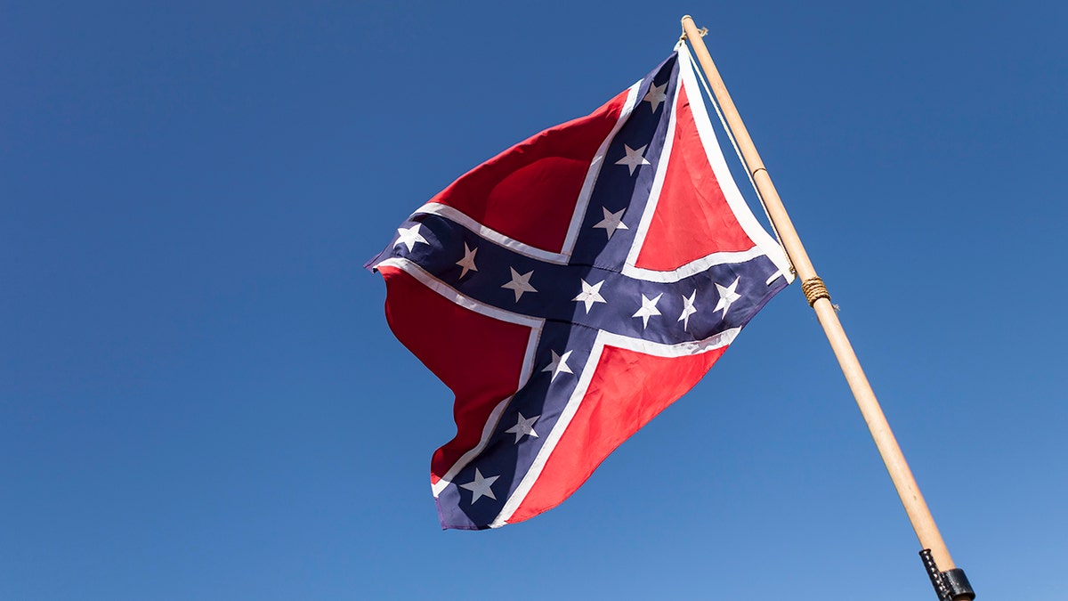 Confederate Flag on pole over blue sky.