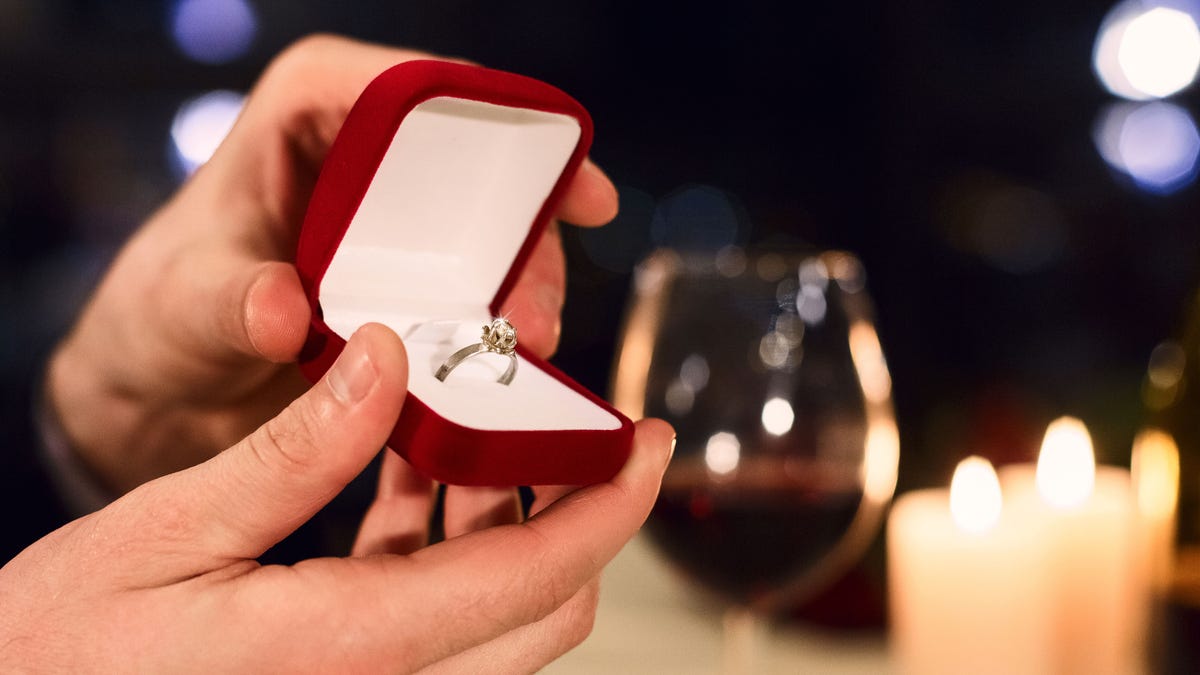 A man holds an engagement ring in a red box.