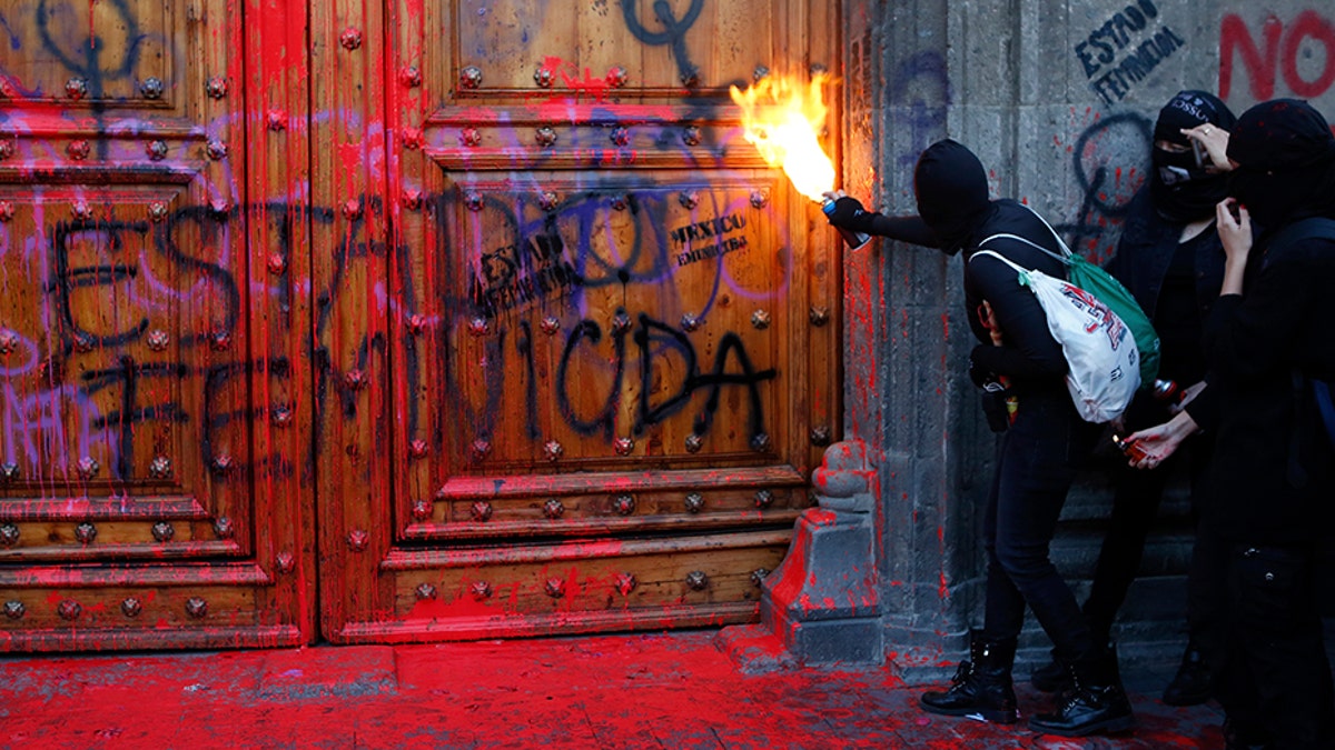 A masked protester sprays fire at the entrance to the National Palace, the presidential office and residence, after demonstrators covered it in fake blood and the Spanish message: "Femicide State," in Mexico City on Friday. (AP)
