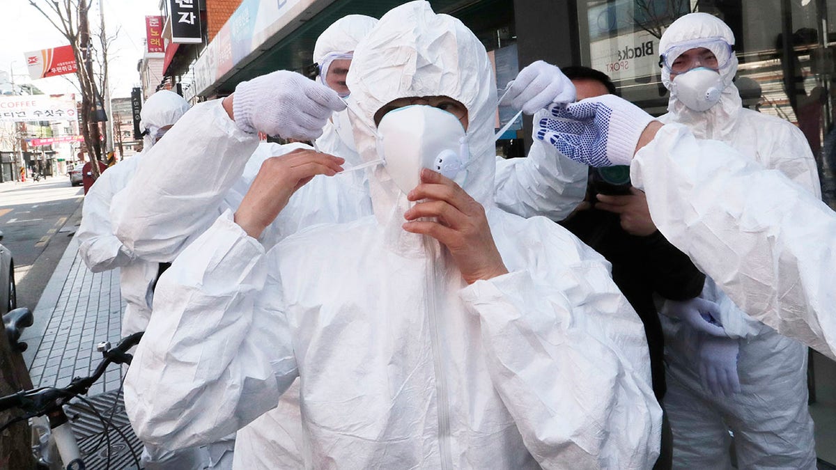 A worker wears a face mask to spray disinfectant as a precaution against the coronavirus at a shopping street in Seoul, South Korea, Thursday, Feb. 27, 2020. South Korea and China each reported hundreds more virus cases Thursday as the new illness persists in the worst-hit areas and spreads beyond borders.