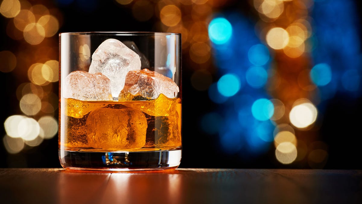 Glass of whiskey with ice on colorful Christmas lights bokeh background