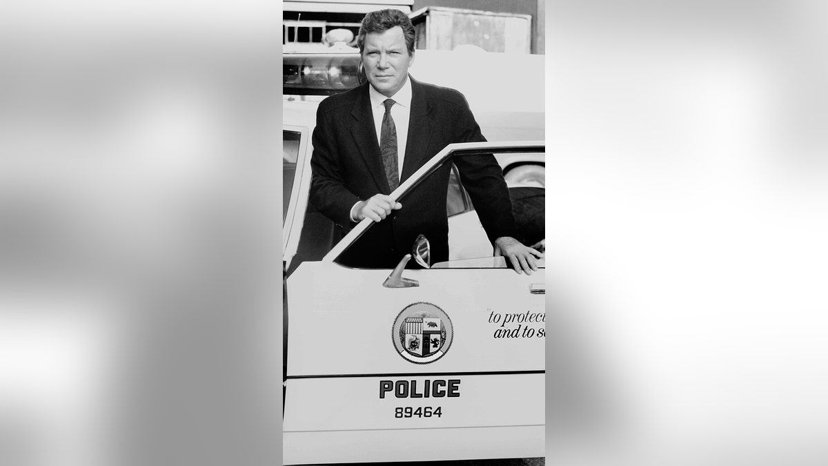 William Shatner stands behind the door of a police car as he hosts the CBS Television true crime program 'Rescue 911.'