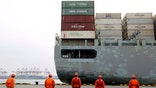 In this Tuesday, Feb. 4, 2020, photo, workers watch a container ship arrive at a port in Qingdao in east China's Shandong province. China cut tariffs on $75 billion of U.S. imports including auto parts on Thursday, Feb. 6 in response to American reductions as part of their truce in a trade war. (Chinatopix via AP)