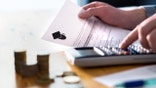 Man counting college savings fund, tuition fee or student loan with calculator. Education price and expenses concept. Money and papers on table. Calculating budget and planning finance.