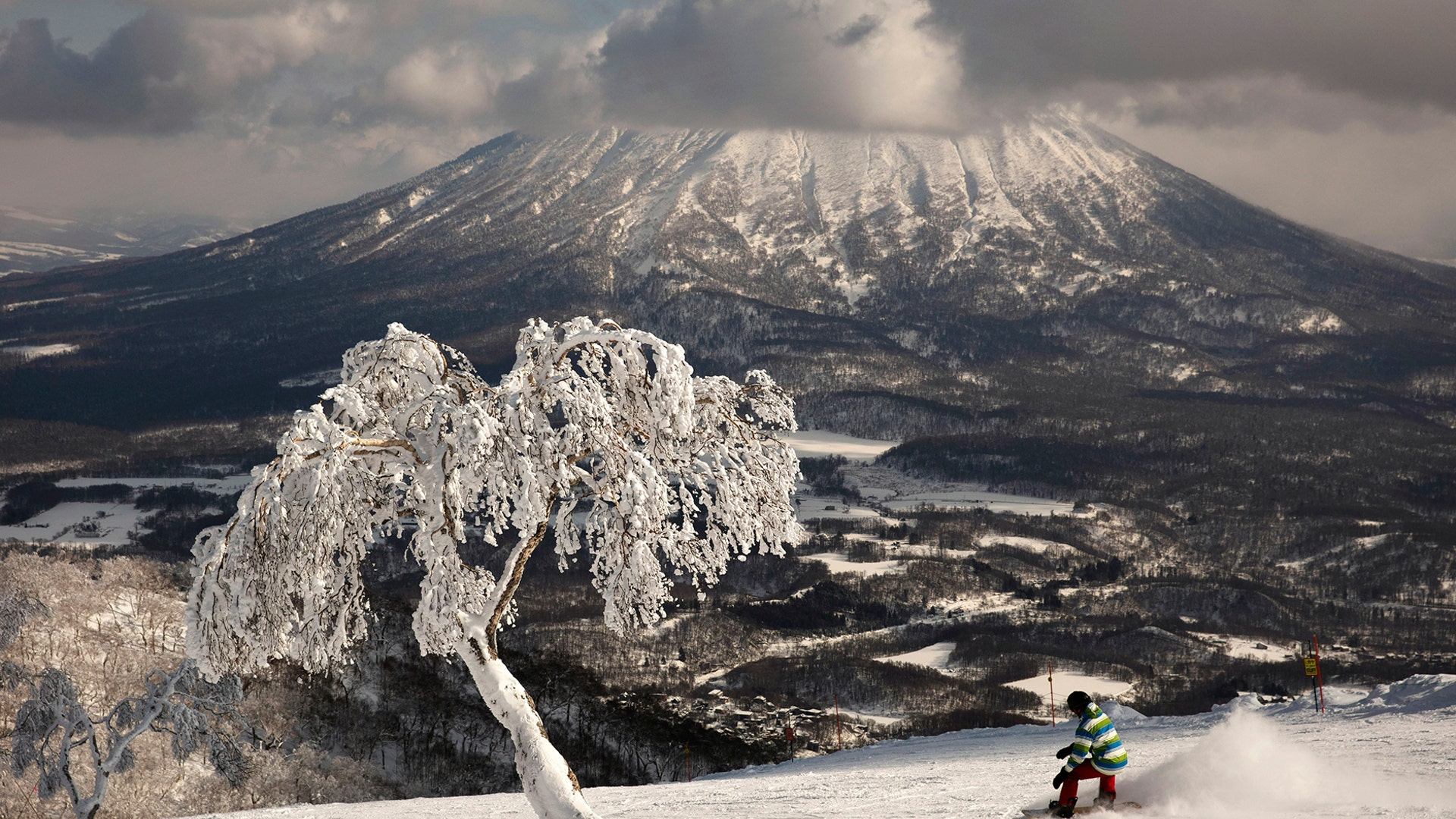 A man snowboards down a slope overlooking Mount Yotei at a ski resort in Niseko, Hokkaido, Japan, Feb. 5, 2020.