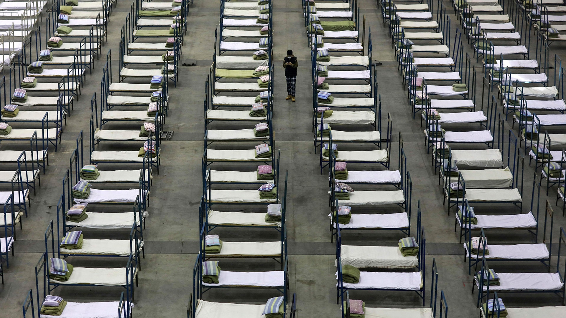 A worker walks among beds in a convention center that has been converted into a temporary hospital in Wuhan, China, Feb. 4, 2020.