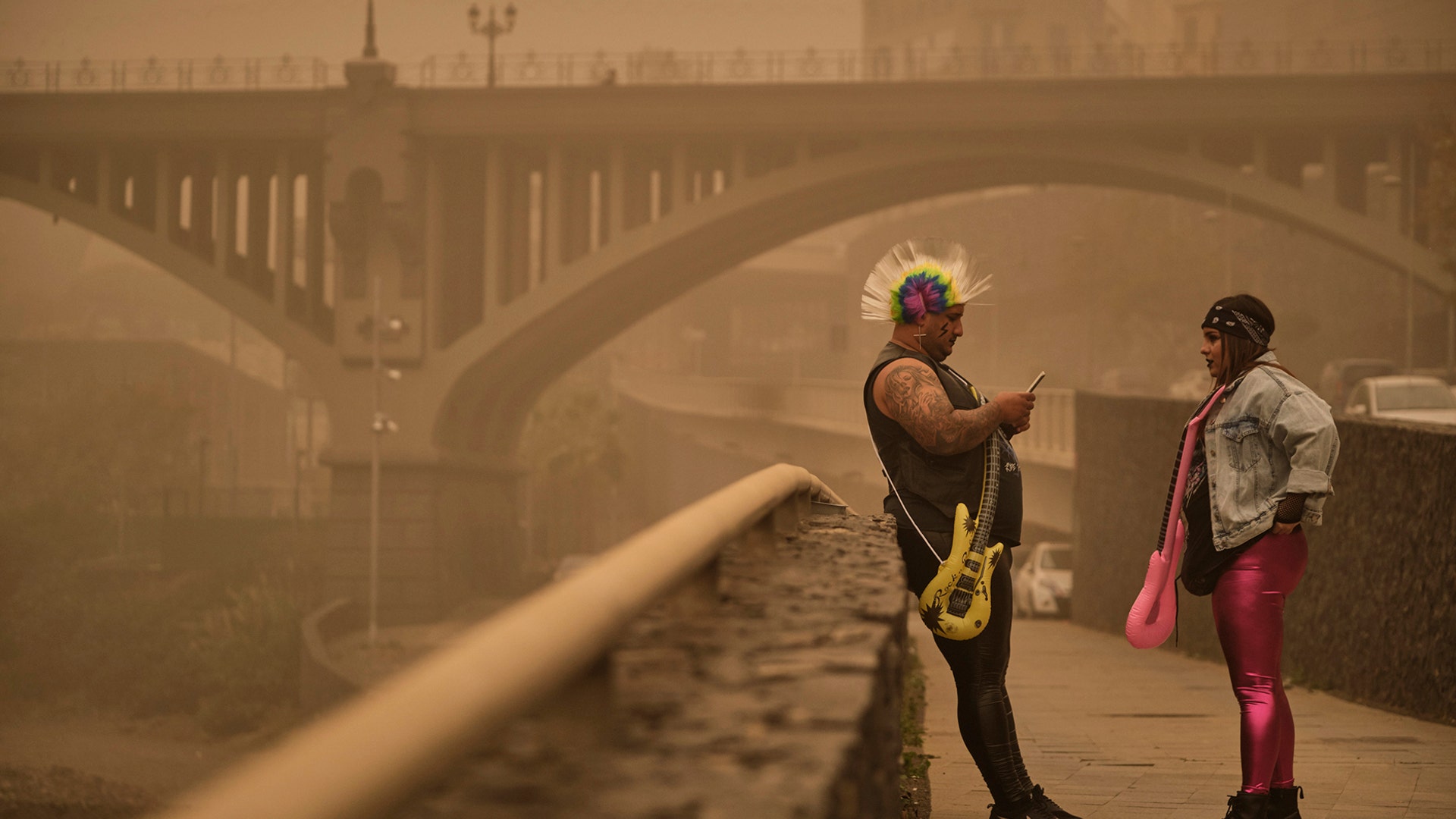 Two people dressed in carnival costumes stand beneath a cloud of red dust in Santa Cruz de Tenerife, Spain, Feb. 23, 2020. 