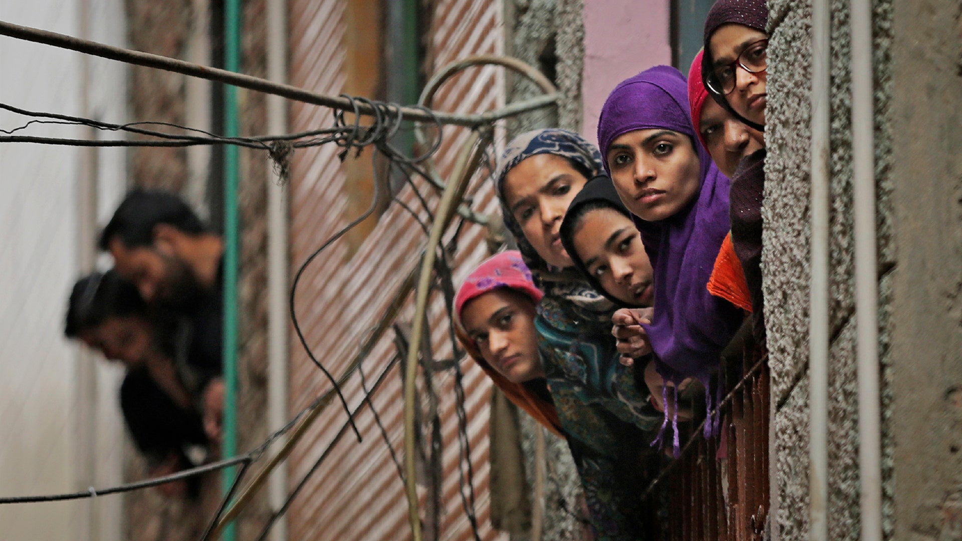 Indian Muslim women look out of a window as security officers patrol a street in New Delhi, India, Feb. 26, 2020. 