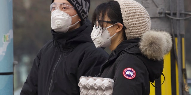 Residents wearing masks wait at a traffic light in Beijing, China Thursday, Feb. 13, 2020. China is struggling to restart its economy after the annual Lunar New Year holiday was extended to try to keep people home and contain novel coronavirus. Traffic remained light in Beijing, and many people were still working at home. (AP Photo/Ng Han Guan)