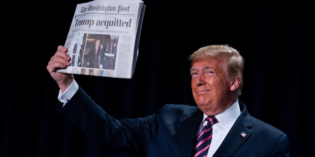 President Donald Trump holds up a newspaper with the headline that reads