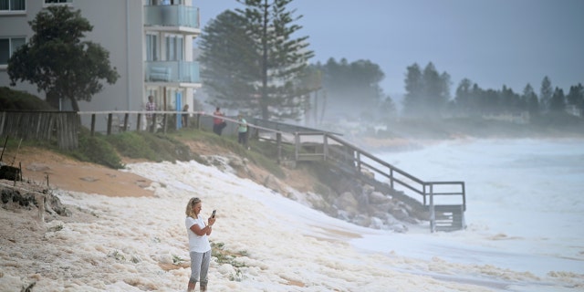 A resident inspects sea foam brought by waves approaching on beach front houses after heavy rain and storms at Collaroy in Sydney's Northern Beaches, Monday, February 10, 2020.