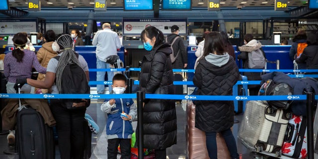 Travelers wearing face masks line up to check in for an American Airlines flight to Los Angeles at Beijing Capital International Airport in Beijing on Jan. 30. (AP Photo/Mark Schiefelbein)