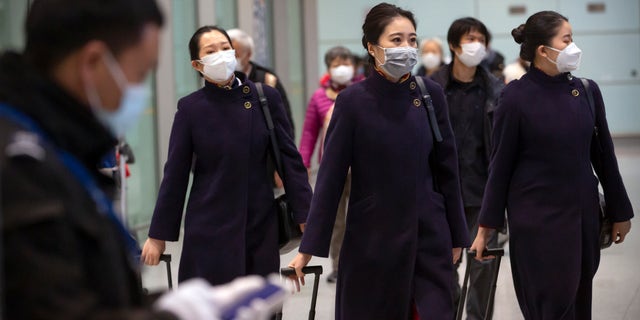 Flight crew members wearing face masks walk through the international arrivals area at Beijing Capital International Airport on Jan. 30. (AP Photo/Mark Schiefelbein)