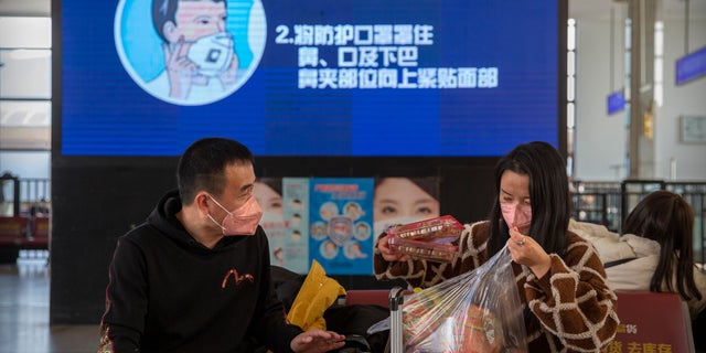 Travelers wear face masks as a screen shows a video about the proper way to wear a mask at the Beijing Railway Station in Beijing, Friday, Jan. 31. (AP Photo/Mark Schiefelbein)